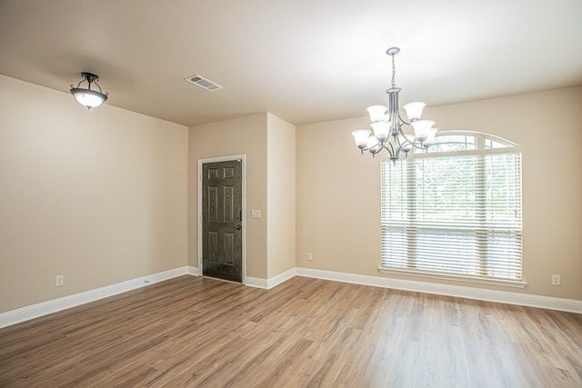 spare room with a chandelier, baseboards, visible vents, and wood finished floors
