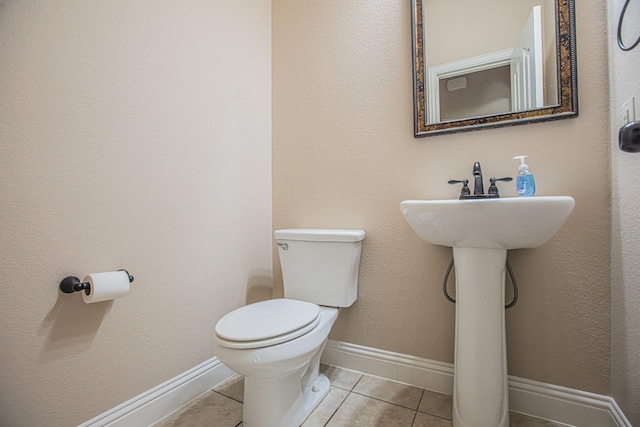 half bathroom with toilet, tile patterned floors, and baseboards