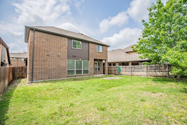 rear view of property with a fenced backyard, a yard, and brick siding