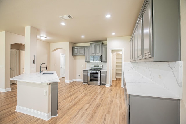 kitchen featuring gray cabinets, visible vents, appliances with stainless steel finishes, arched walkways, and a sink