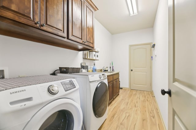 laundry area featuring a sink, washing machine and dryer, cabinet space, and light wood-style flooring