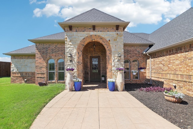 property entrance with stone siding, brick siding, a yard, and roof with shingles