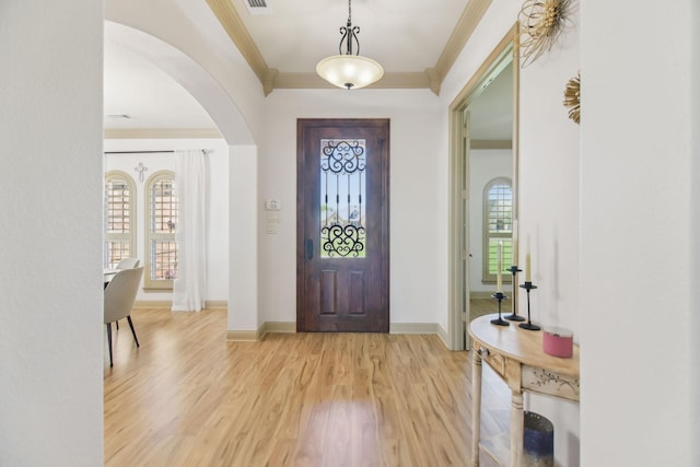 entryway featuring crown molding, arched walkways, light wood-style flooring, and baseboards