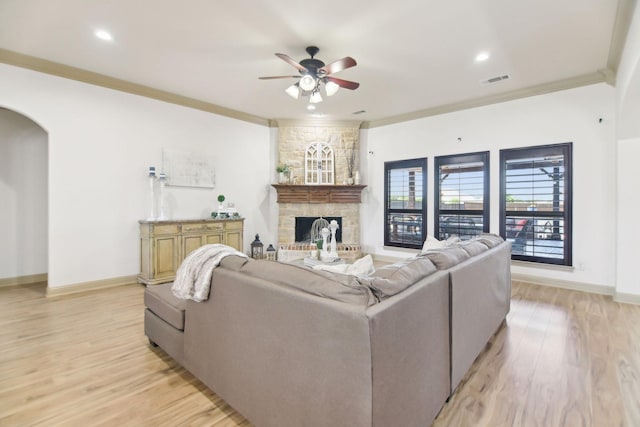 living area with arched walkways, ornamental molding, a stone fireplace, light wood finished floors, and a ceiling fan