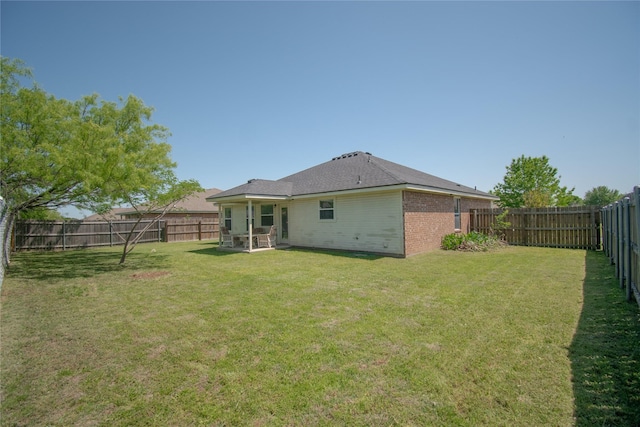 back of house with brick siding, a yard, and a fenced backyard