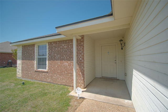 doorway to property with a lawn and brick siding