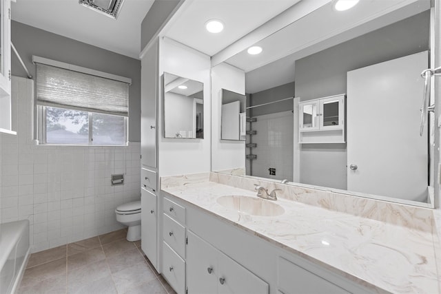 full bathroom featuring a tile shower, tile patterned floors, toilet, vanity, and tile walls