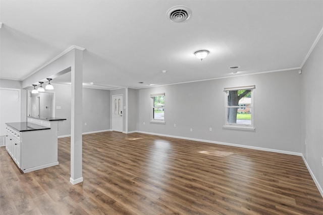 unfurnished living room with a wealth of natural light, ornamental molding, visible vents, and baseboards