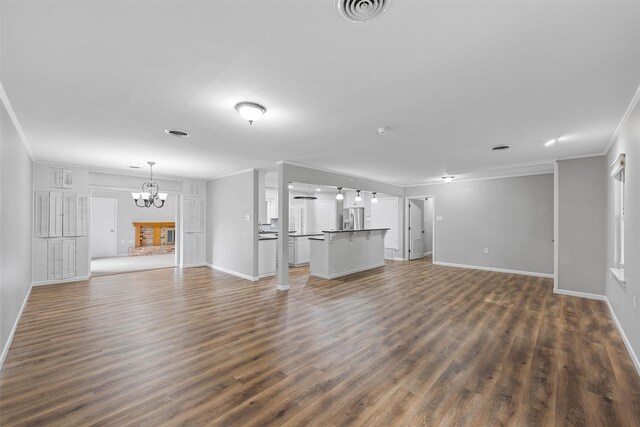 unfurnished living room featuring dark wood finished floors, visible vents, ornamental molding, baseboards, and a notable chandelier