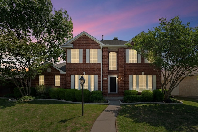 colonial inspired home featuring brick siding and a front yard