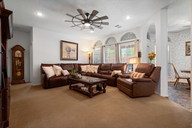living room with a textured ceiling, visible vents, light colored carpet, and ceiling fan