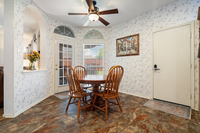 dining space with stone finish floor, wallpapered walls, and arched walkways