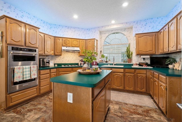 kitchen with under cabinet range hood, wallpapered walls, double oven, and a sink