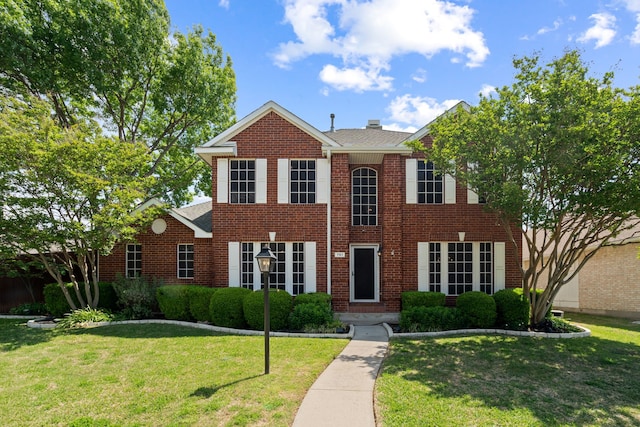 colonial-style house featuring brick siding, a chimney, and a front lawn