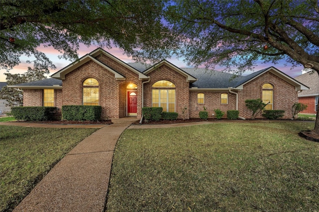 ranch-style house featuring brick siding, a yard, and roof with shingles