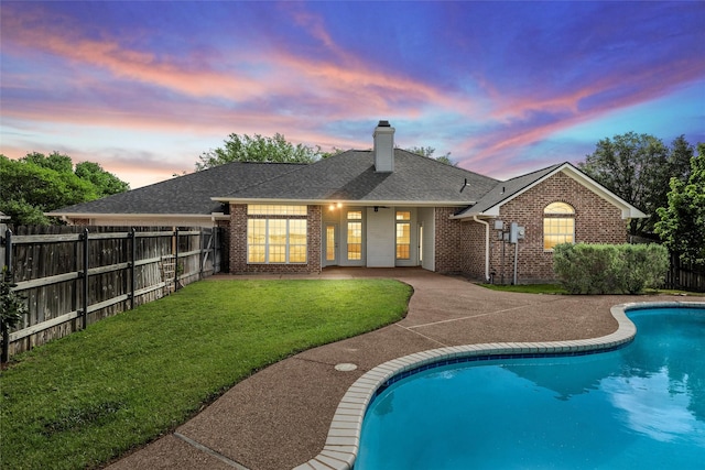 back of property with a chimney, fence, a yard, a fenced in pool, and brick siding