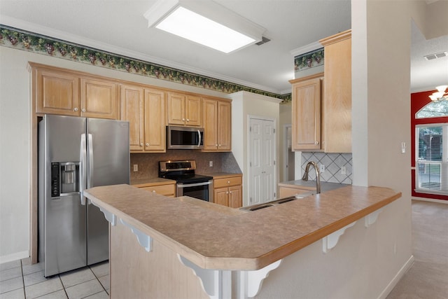 kitchen with a peninsula, a sink, appliances with stainless steel finishes, a breakfast bar, and ornamental molding