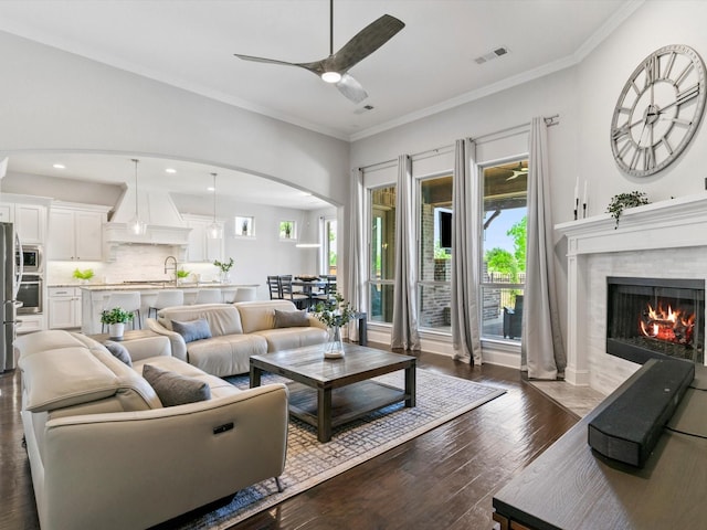 2908 Ballater Ct, The Colony, TX 75056 - living room with healthy amount of natural light, ceiling fan, arched walkways, a fireplace with flush hearth, and ornamental molding