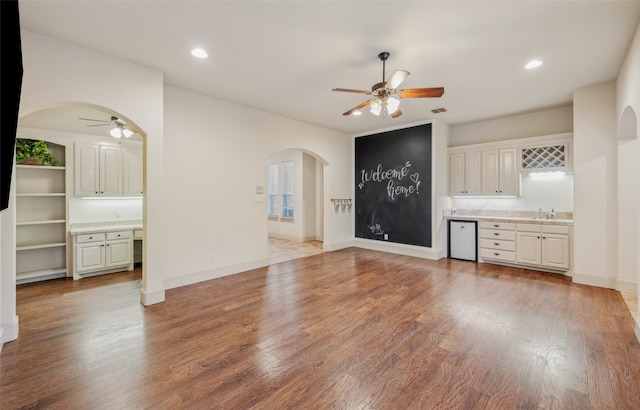 unfurnished living room featuring arched walkways, a sink, and a ceiling fan