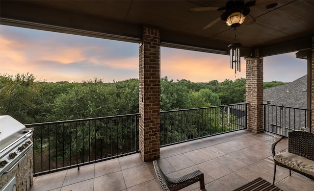 balcony at dusk with a ceiling fan, a view of trees, and area for grilling
