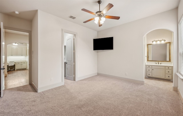 unfurnished bedroom with a sink, arched walkways, connected bathroom, and light colored carpet