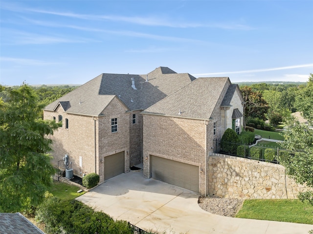 view of side of home with central air condition unit, brick siding, concrete driveway, an attached garage, and a shingled roof