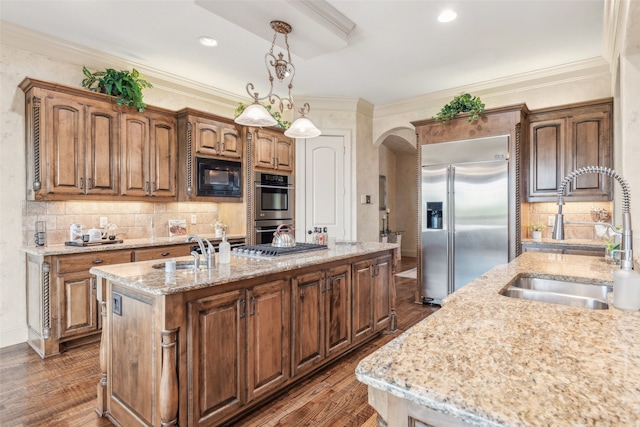 kitchen featuring an island with sink, a sink, built in appliances, and crown molding