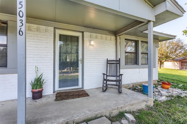 view of exterior entry with brick siding and a porch