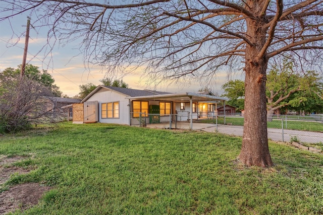 back of house at dusk featuring a gate, a yard, driveway, fence private yard, and an attached carport