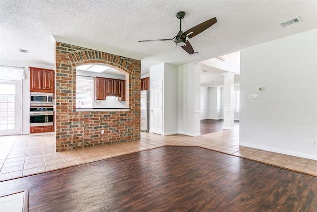 unfurnished living room featuring a ceiling fan, visible vents, a healthy amount of sunlight, and light wood-style floors