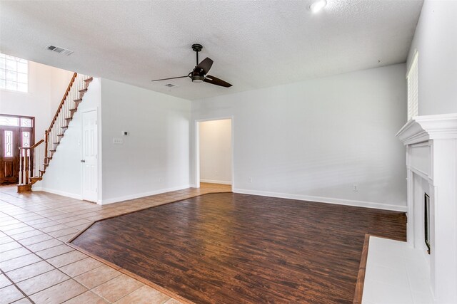 unfurnished living room featuring visible vents, stairs, a fireplace, ceiling fan, and a textured ceiling
