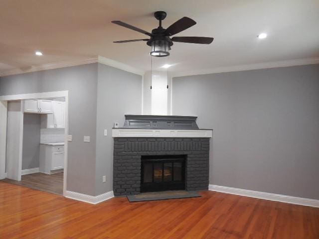 unfurnished living room featuring a ceiling fan, crown molding, a brick fireplace, and light wood-type flooring