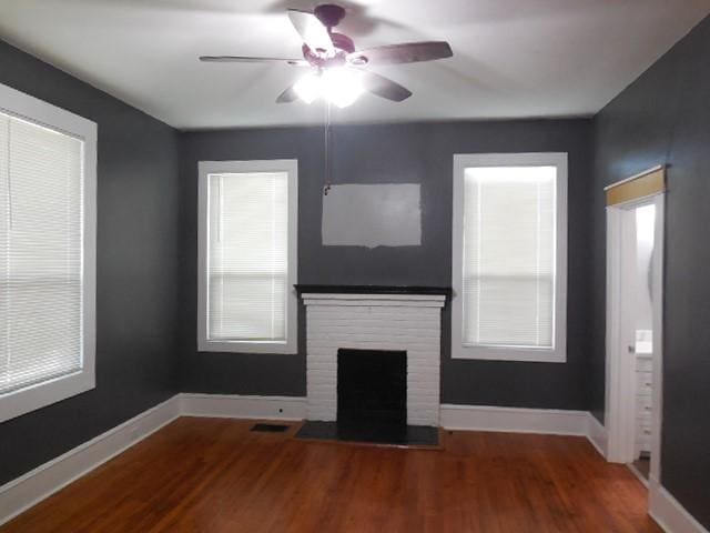 unfurnished living room featuring wood finished floors, a brick fireplace, baseboards, and ceiling fan