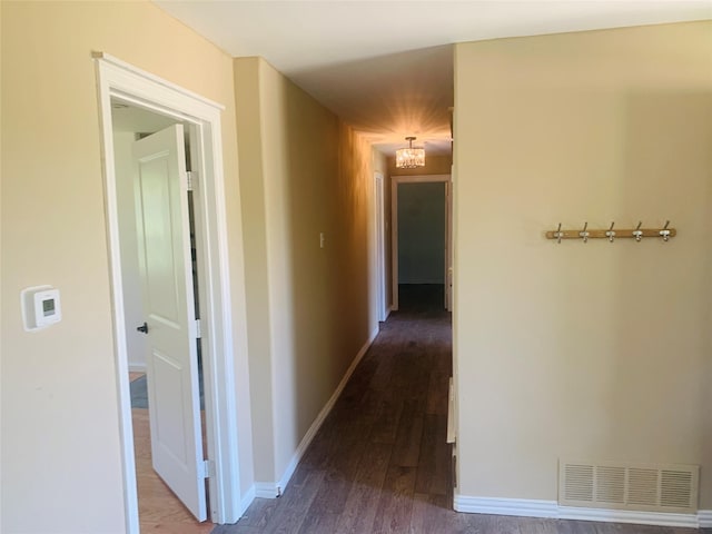 hall with baseboards, wood finished floors, visible vents, and an inviting chandelier