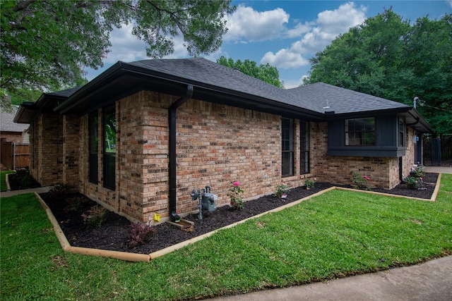view of property exterior with brick siding, a lawn, fence, and roof with shingles