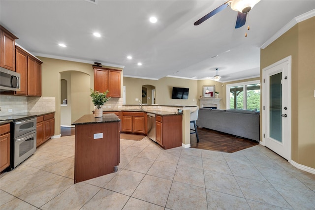 kitchen featuring arched walkways, ceiling fan, crown molding, and stainless steel appliances