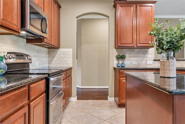 kitchen with arched walkways, dark stone counters, tasteful backsplash, light tile patterned flooring, and appliances with stainless steel finishes