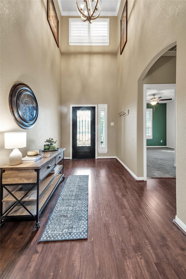 foyer entrance featuring a towering ceiling, wood finished floors, baseboards, and arched walkways