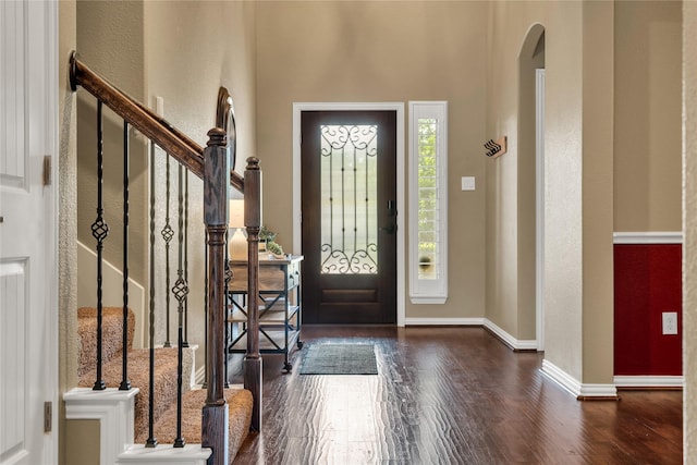 entryway with arched walkways, a towering ceiling, baseboards, wood finished floors, and a textured wall