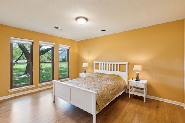 bedroom with baseboards, wood finished floors, and visible vents