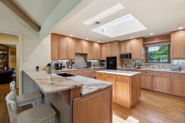kitchen featuring a sink, a skylight, black appliances, a breakfast bar, and visible vents
