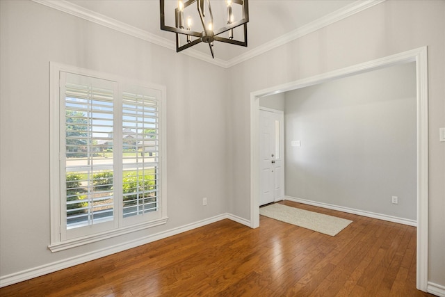 empty room featuring hardwood / wood-style flooring, an inviting chandelier, ornamental molding, and a healthy amount of sunlight