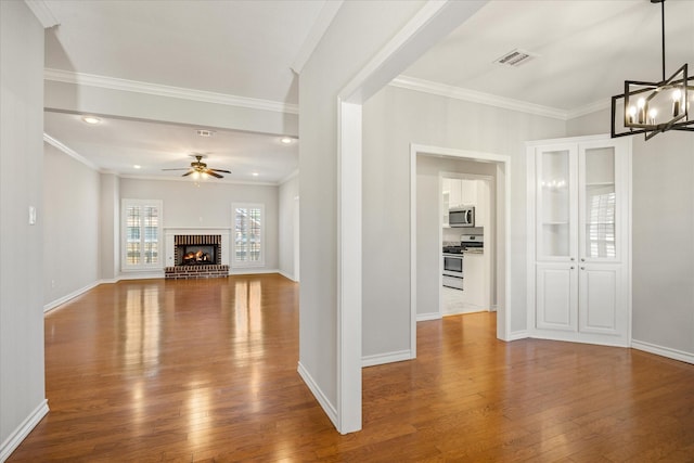 unfurnished living room with visible vents, wood-type flooring, crown molding, baseboards, and ceiling fan with notable chandelier