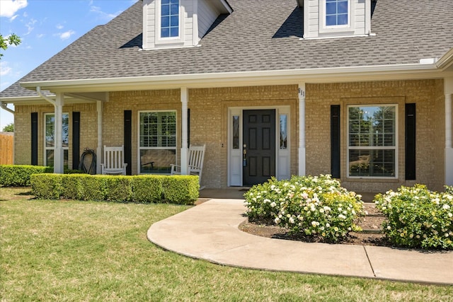 entrance to property featuring a lawn, brick siding, a porch, and a shingled roof