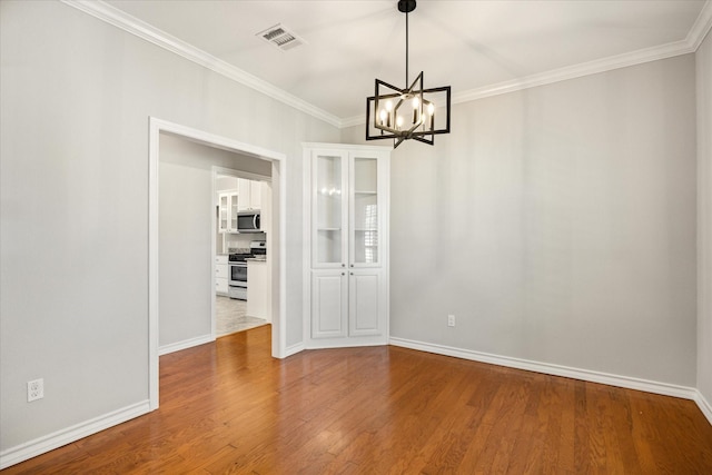 unfurnished dining area with an inviting chandelier, wood finished floors, visible vents, crown molding, and baseboards