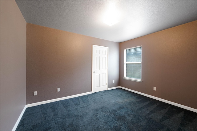 empty room featuring dark carpet, a textured wall, and baseboards
