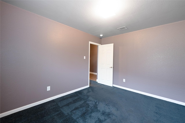 unfurnished room with visible vents, dark colored carpet, and baseboards