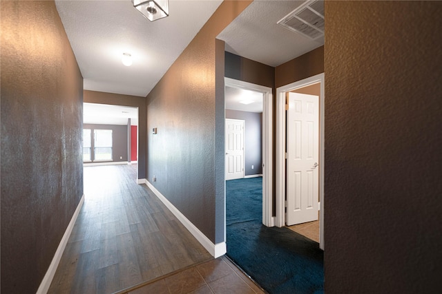 corridor featuring baseboards, a textured wall, tile patterned floors, and visible vents