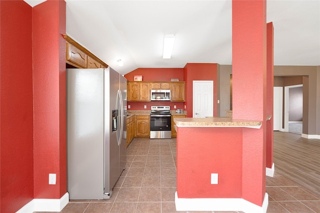 kitchen with light tile patterned flooring, stainless steel appliances, light countertops, a peninsula, and lofted ceiling