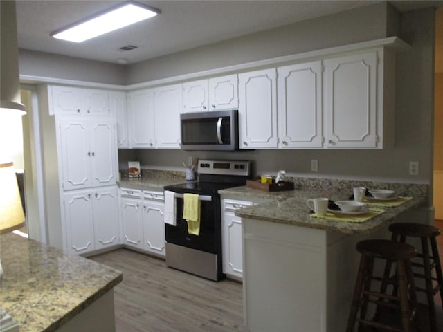 kitchen with stainless steel appliances, a peninsula, light wood-style floors, white cabinetry, and a breakfast bar